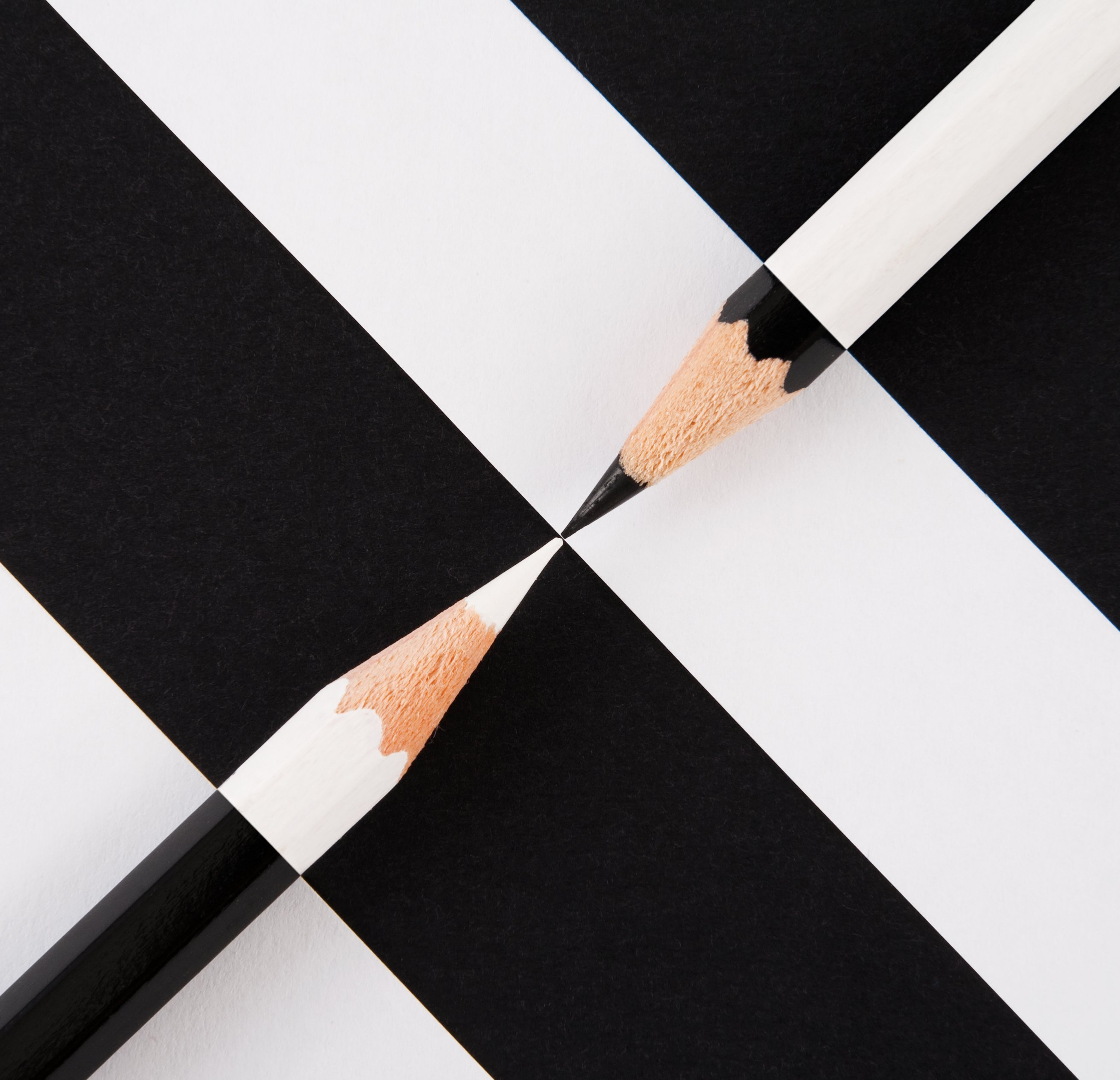 A black pencil and white pencil pointing at each other on a black and white background