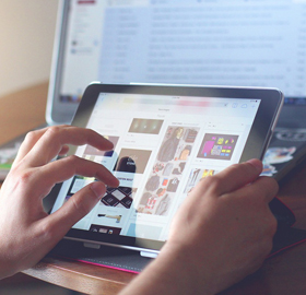 A person using a tablet with a computer monitor in the background
