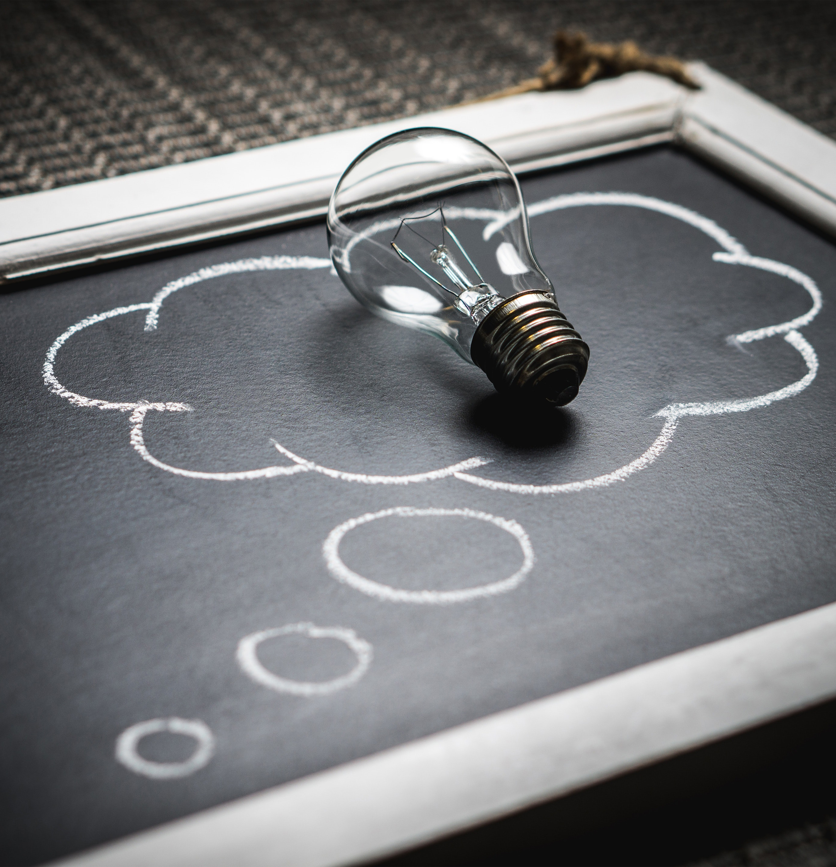 A chalkboard with a light bulb laying on a thought bubble