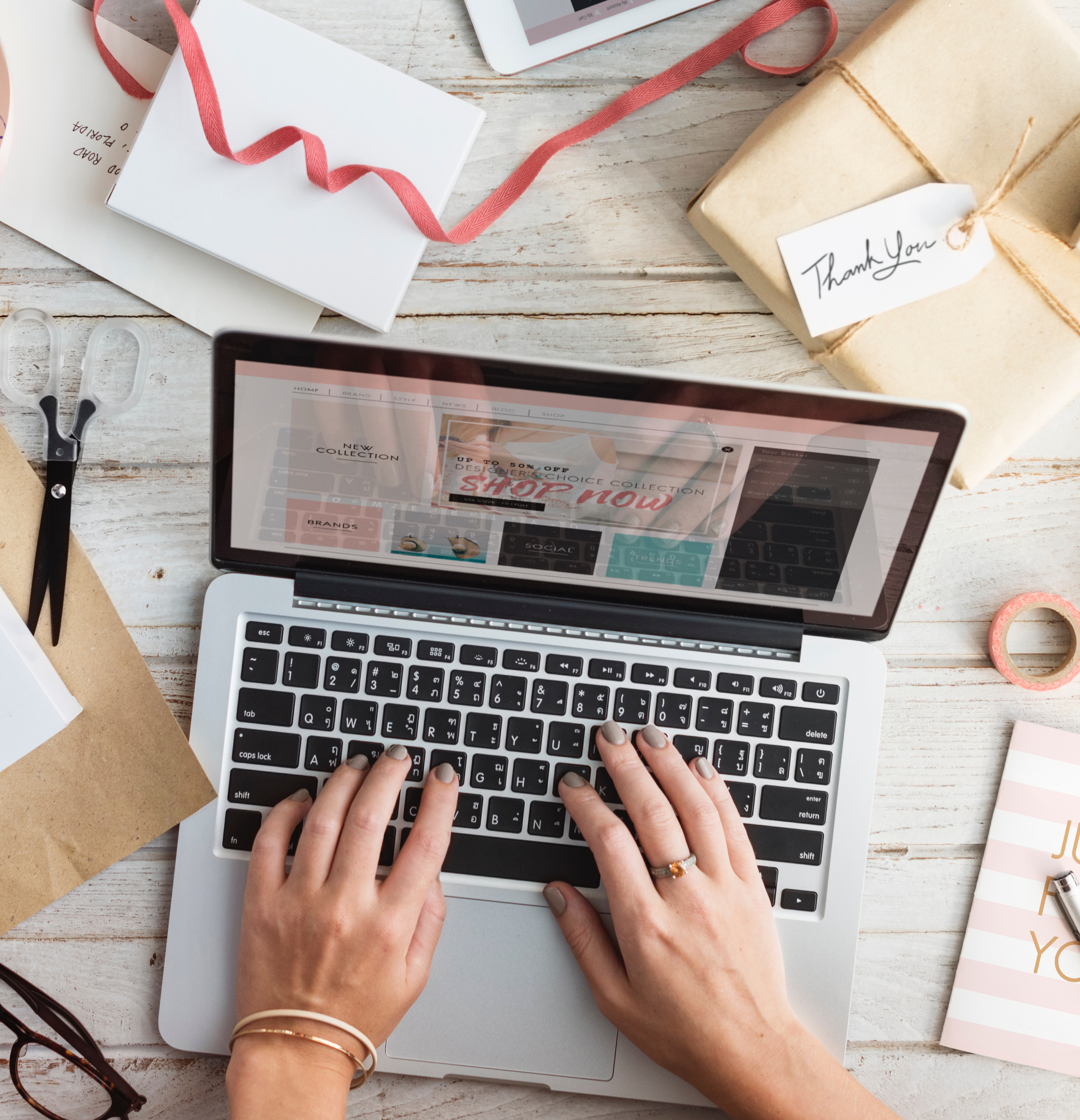 A person typing on a computer surrounded by craft supplies and scissors