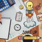 Image of a calculator, ledger, notepad and an illustrated lightbulb taking off for a business startup