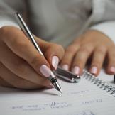 close up of hands writing in notebook with fountain pen