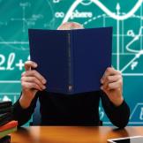 child holding book sitting in front of chalk board with science and math symbols