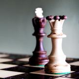 A photograph of a wooden king and queen on a chess board