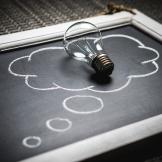 A chalkboard with a light bulb laying on a thought bubble