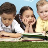 A girl and two boys reading open books laying on the grass