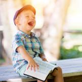An image of a laughing child who is reading a book