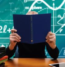 child holding book sitting in front of chalk board with science and math symbols